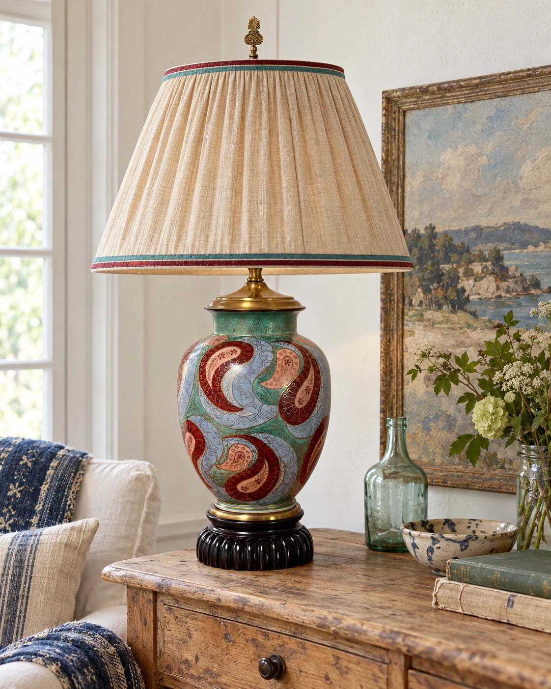Paisley ceramic lamp shown with a red-and-green-trimmed cream shade.